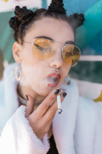 Close-up of young woman smoking cigarette by graffiti wall