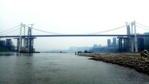 Suspension bridge in city against clear sky