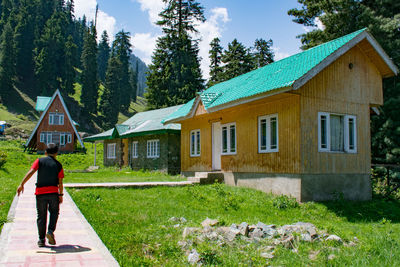 Rear view of woman walking on footpath by building against sky