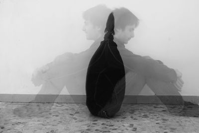 Rear view of woman sitting on wall during foggy weather