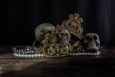 Close-up of human skulls and gold jewelry on table against black background