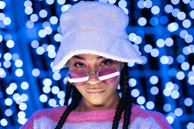 Joyful woman of color with a white beanie braided hairstyle and pink glasses enjoying the christmas