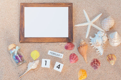 High angle view of empty picture frame and seashells on sand at beach