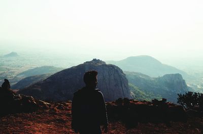 Rear view of man standing on mountain against clear sky