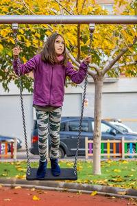 Full length of girl standing on swing in playground