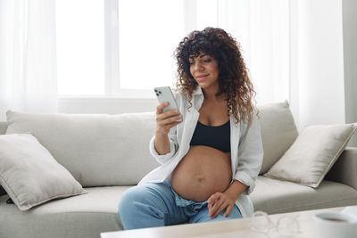 Young woman using mobile phone while lying on sofa at home