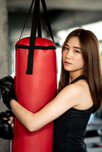 Portrait of confident young woman holding punching bag while standing in gym