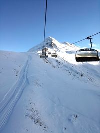 Ski lifts over snow covered mountain against clear blue sky