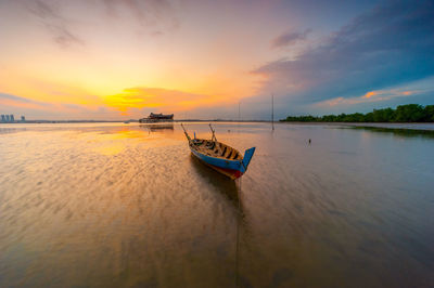 Boat moored in sea against sky during sunset