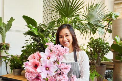 Portrait of smiling young woman by pink potted plants