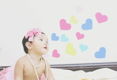 Shirtless baby girl looking away while sitting on bed at home