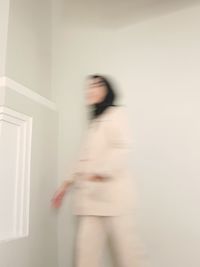 Blurred motion of woman walking against wall