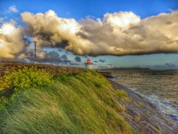 Lighthouse on beach against clouds