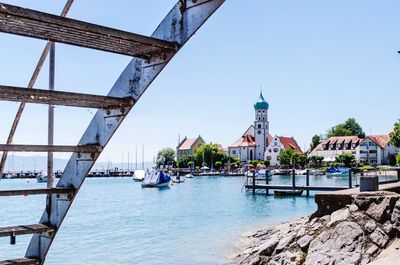 Bridge over river by buildings against clear blue sky