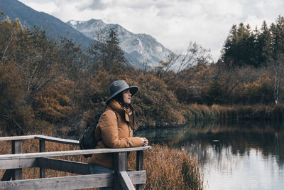 Young woman standing on wooden deck by lake in autumn