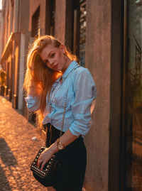 Portrait of young woman standing against building in city