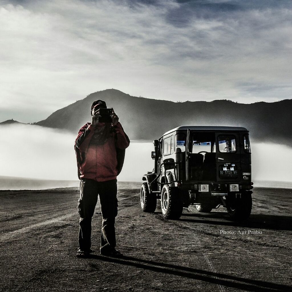 sky, lifestyles, full length, transportation, rear view, mountain, leisure activity, land vehicle, men, mode of transport, photography themes, standing, cloud - sky, casual clothing, travel, camera - photographic equipment, photographing, cloud