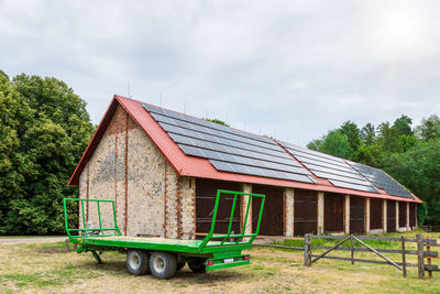 Green farm trailer parked in front of a large barn. solar panels installed on the roof of the barn