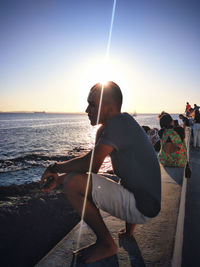 Rear view of people at beach against sky during sunset