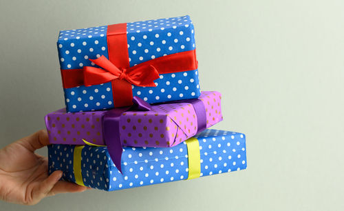 Female hand holding a stack of gift boxes tied with silk ribbon on a gray background, surprise 