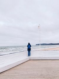 Rear view of man standing on pier over sea against sky