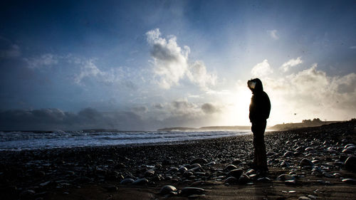 Silhouette man standing on beach against sky during sunset