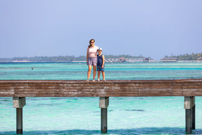 Mother and son crossing a wooden bridge looking the ocean