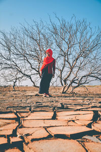 Woman standing by bare tree against sky