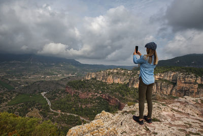 Woman photographing the landscape with her mobile phone, from the top of the mountain.