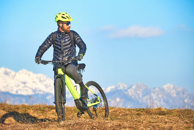 Man riding bicycle on field against sky