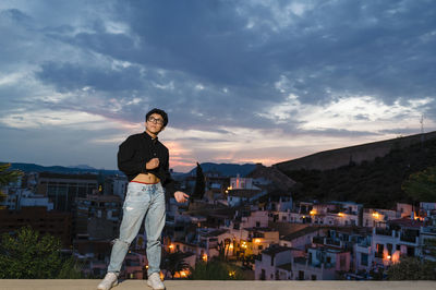 Young transgender man looking up while posing outdoors at sunset.