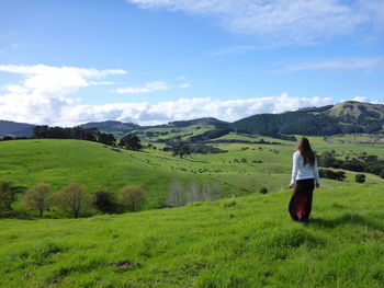 Rear view of woman standing on grassy field against blue sky