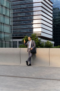 Businessman using smart phone leaning on wall