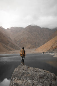 Man standing on rock by mountain against sky