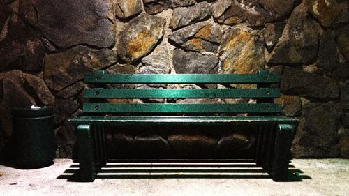 Empty bench against stone wall