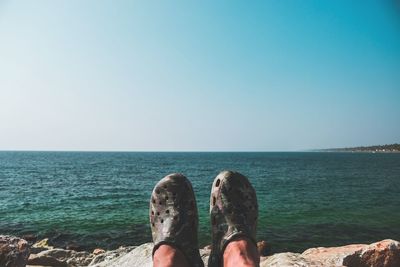 Low section of man in sea against clear sky