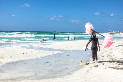Rear view full length of vendor selling cotton candy on shore at beach during sunny day