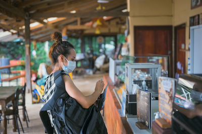 Side view point of young women wearing surgical mask with backpack buying coffee at coffee shop 