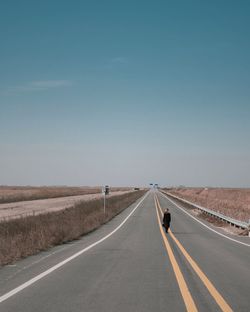 Rear view of young woman standing on road against clear sky during sunny day