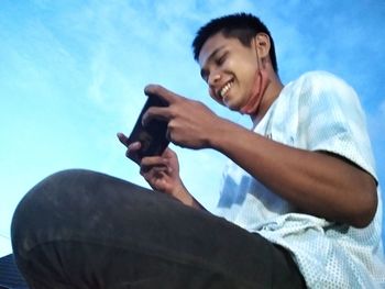 Low angle view of man using mobile phone against sky