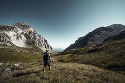 Rear view of man walking on mountain against blue sky during winter