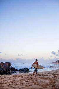 Full length of surfer walking at beach sky