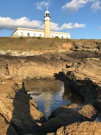 Lighthouse by rocks against sky