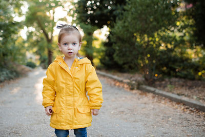 Pretty funny kid girl 2-3 year old wear yellow bright raincoat, rubber boots walk in park 