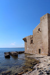 Old building by sea against clear blue sky