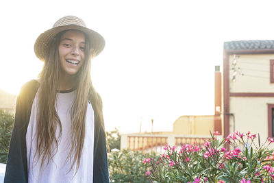 Portrait of smiling young woman standing by flowering plants against sky