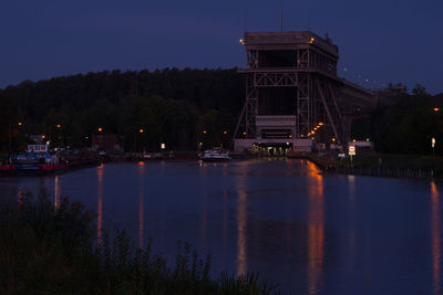 Illuminated city by river against sky at dusk