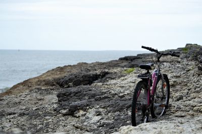 Bicycle on rock by sea against sky