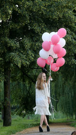Rear view of woman with balloons standing against trees