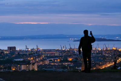 Rear view of man looking at illuminated cityscape against sky